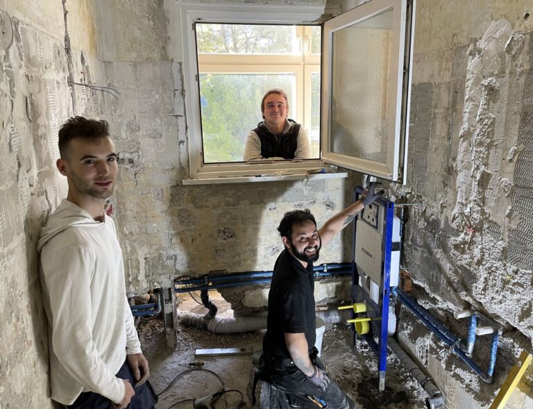 Drei Handwerker auf einer Baustelle aus dem Team der PBG Handwerker GmbH schauen lächelnd in die Kamera